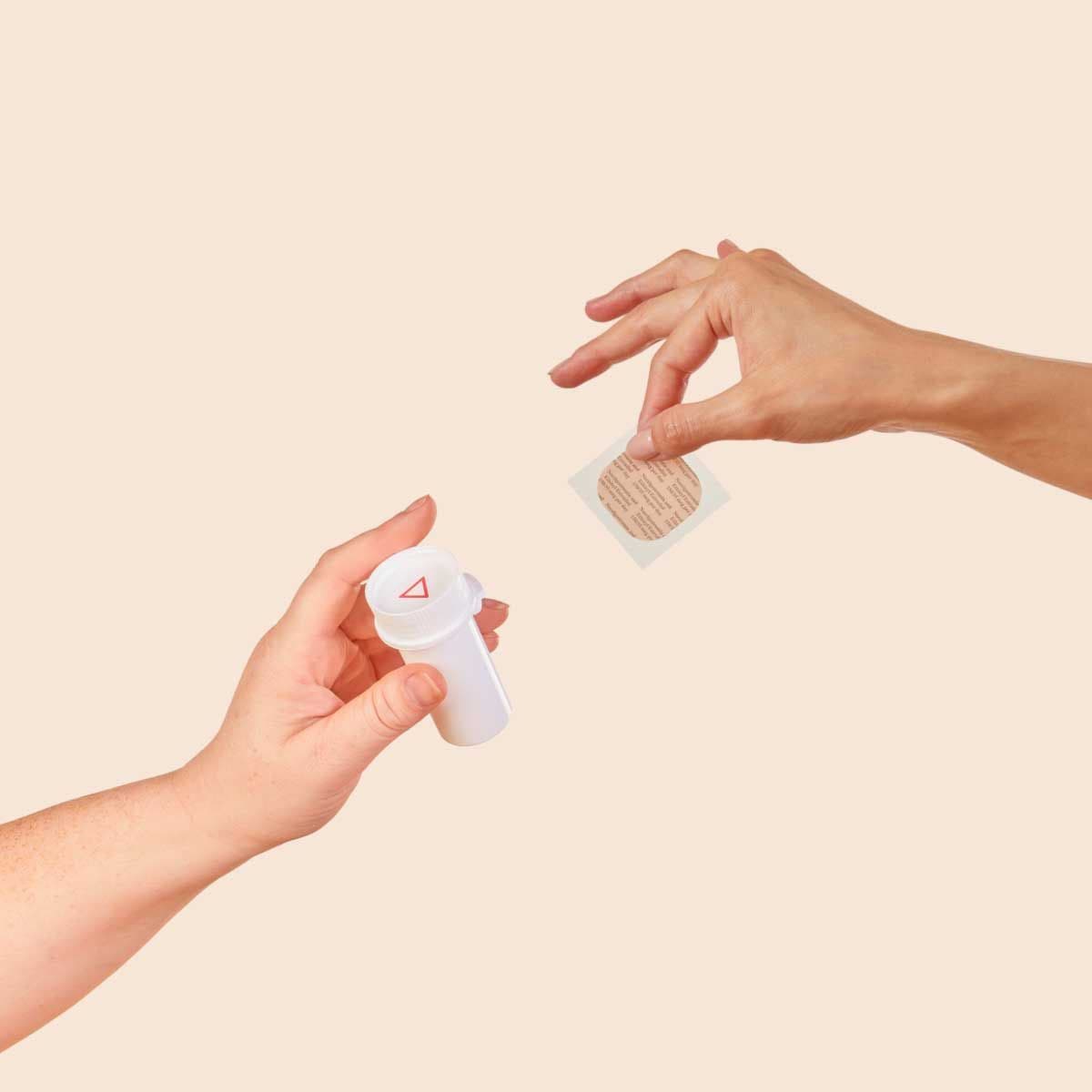 Two hands holding a pill vial and a HRT patch with a cream background