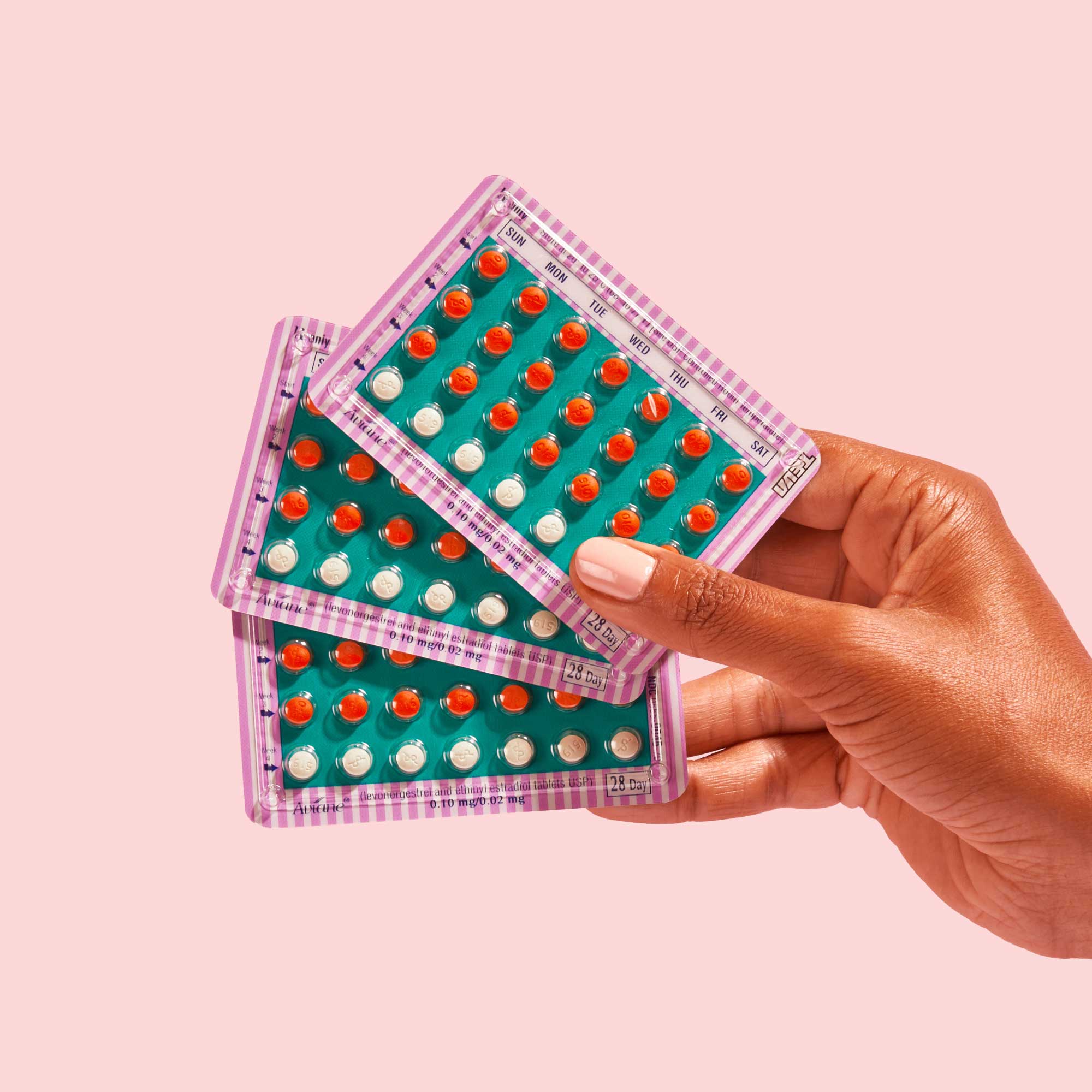 A woman's hand holding 3 birth control pill packets in front of a pink background