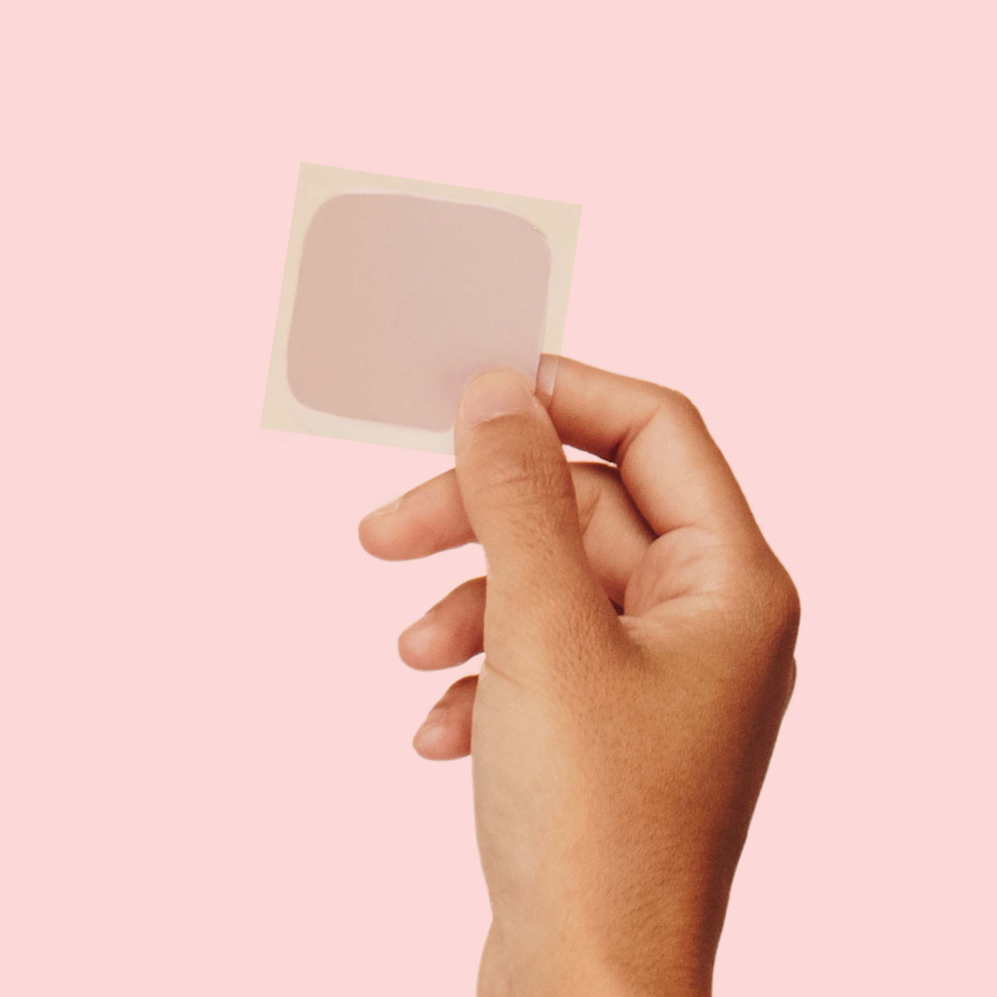 A woman's hand holding a birth control patch in front of a pink background