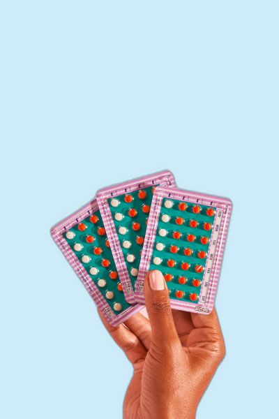 Hand holding 3 packets of birth control on a blue background