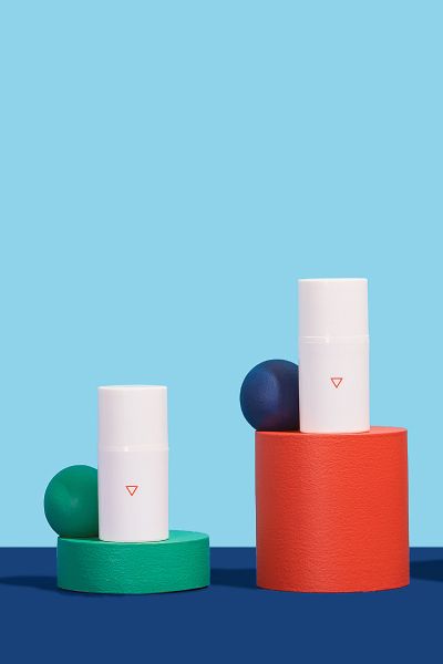 Two bottles of Wisp Hydrocortisone cream balanced on colorful abstract shapes on a blue surface