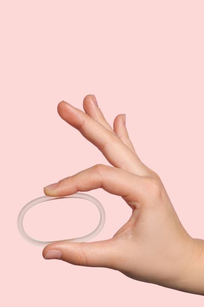 Woman's hand holding NuvaRing Birth Control with a pink background