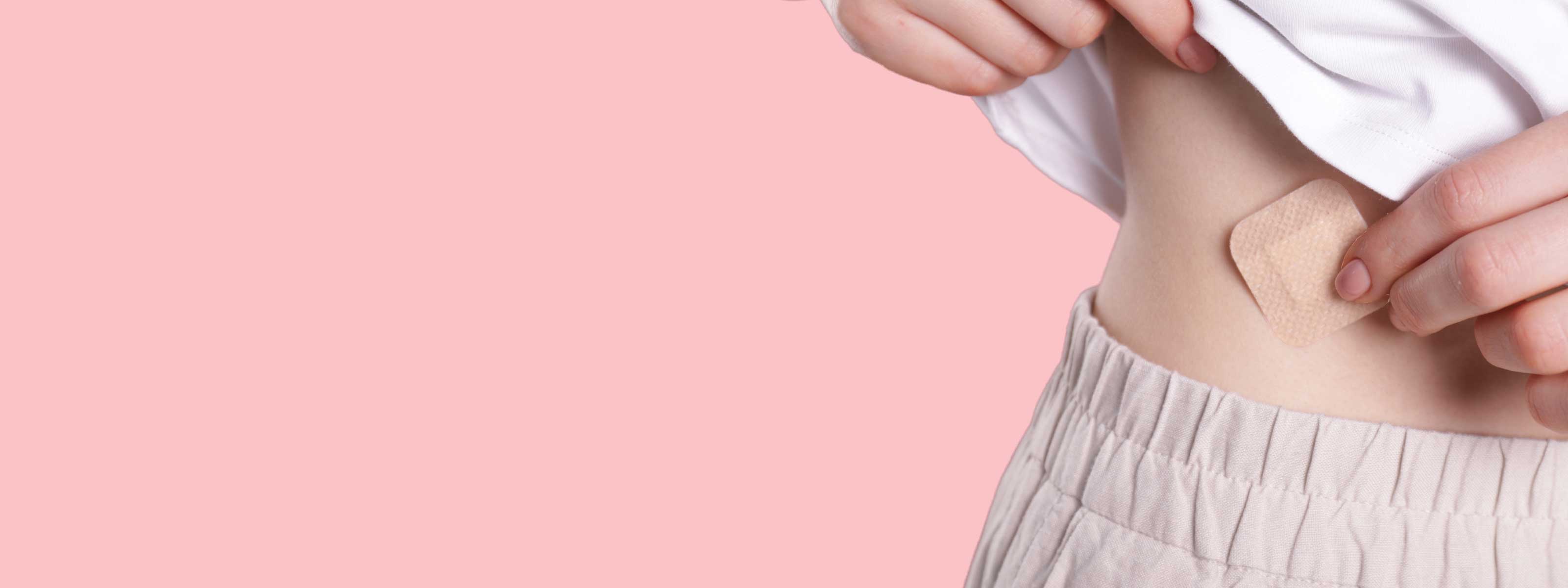 person pressing a birth control patch on their stomach in front of a pink background