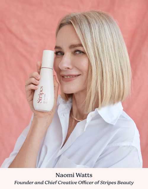 Naomi Watts - Founder of Stripes Beauty wearing a white shirt while holding a Stripes Beauty product in front of a pink background