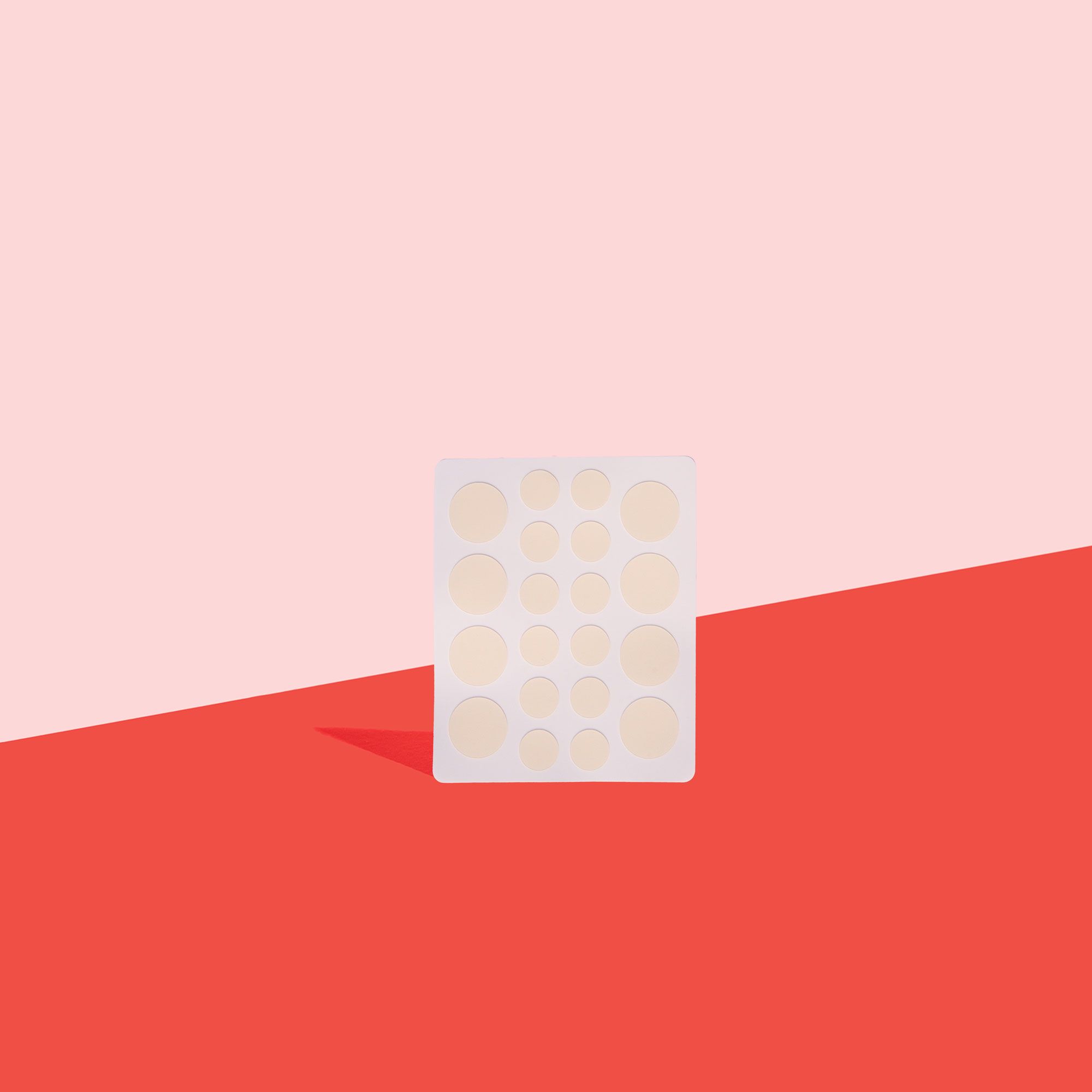 A sheet of 20 hydrocolloid patches in two sizes on a red surface with a pink background