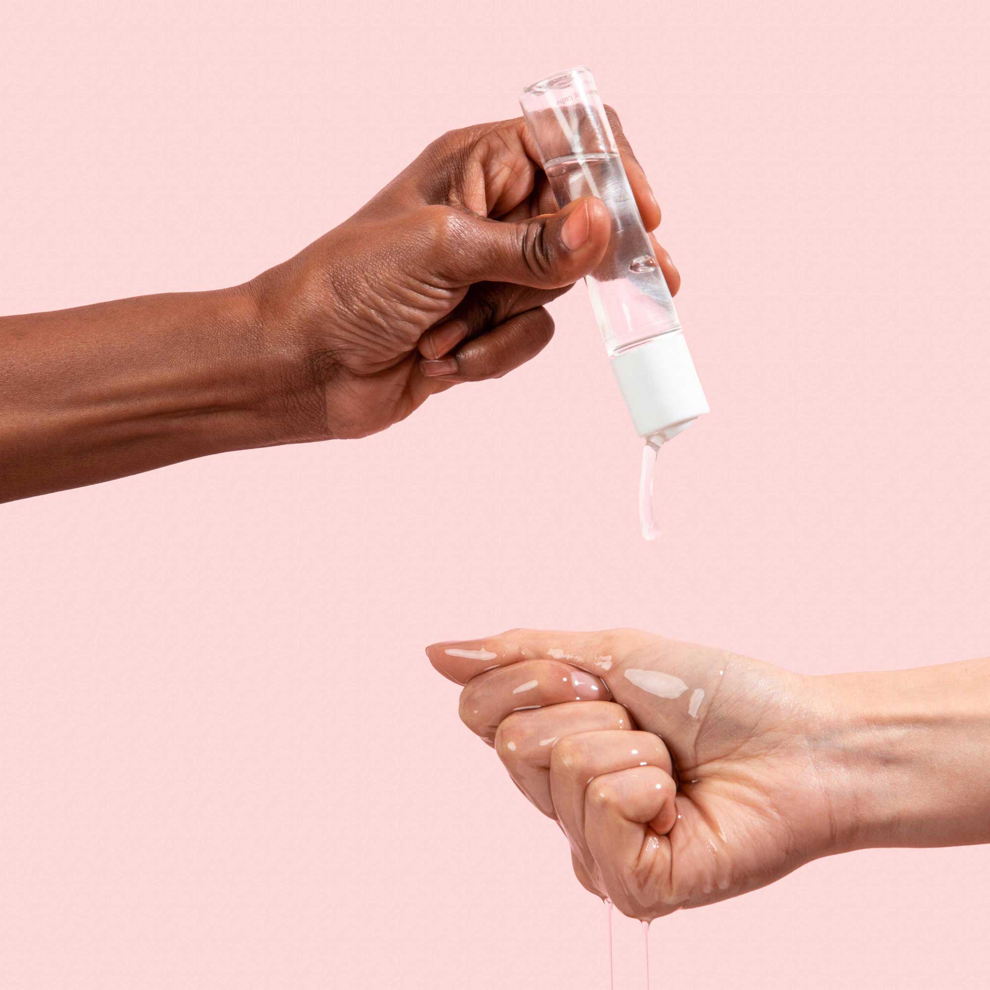 Female hand holding bottle of Wisp Harmonizing Lube and pouring lube onto other hand on pink background