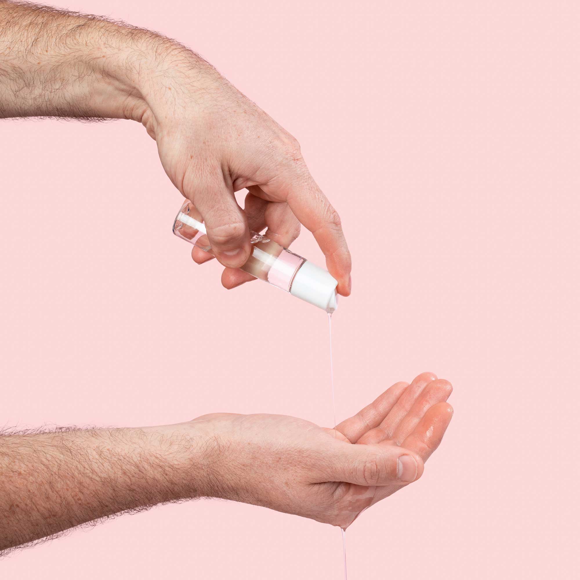 Male hand holding bottle of Wisp Harmonizing Lube and pouring lube into other hand on pink background