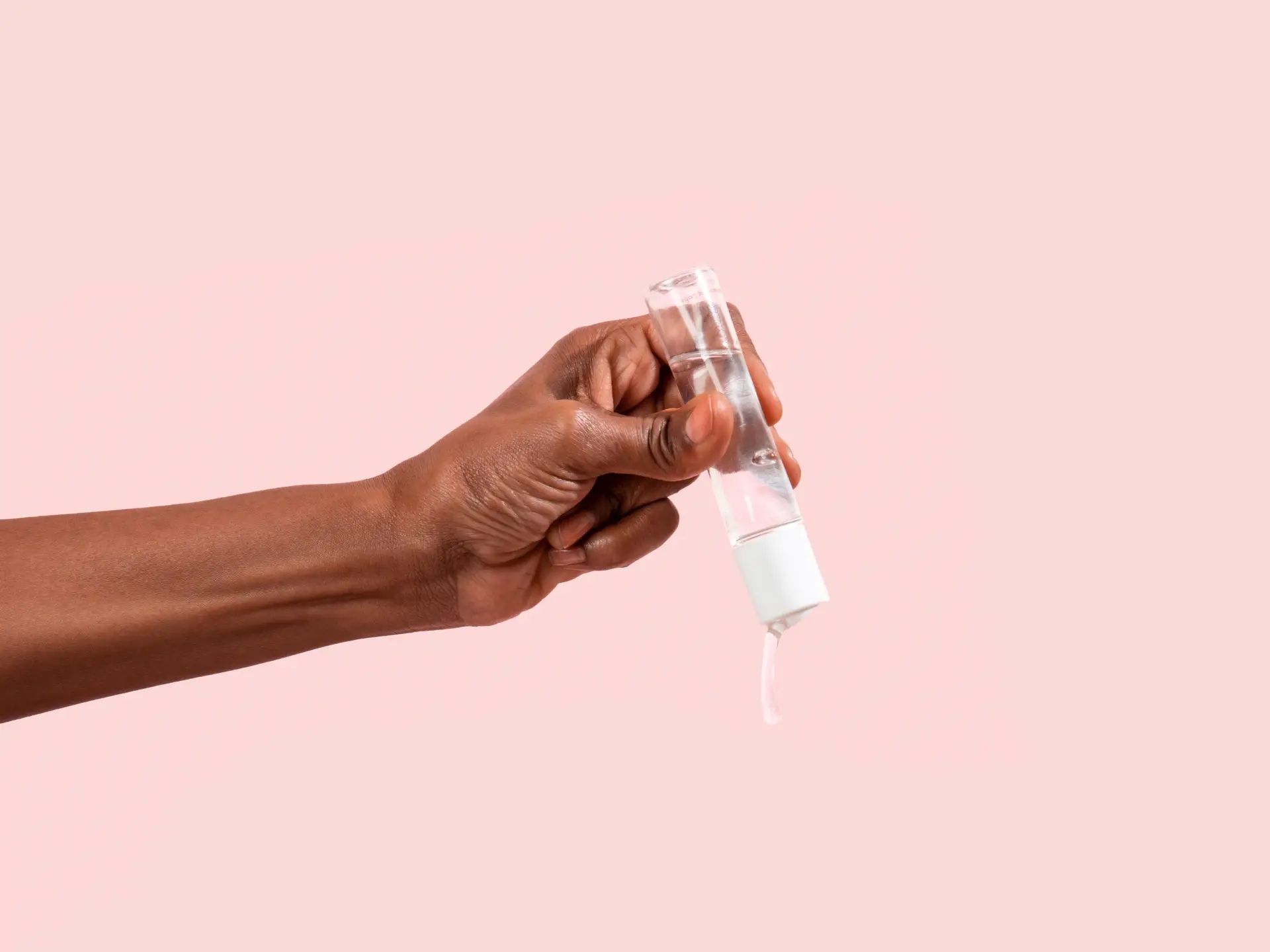 Hand pouring Wisp Harmonizing Lube against a pink background