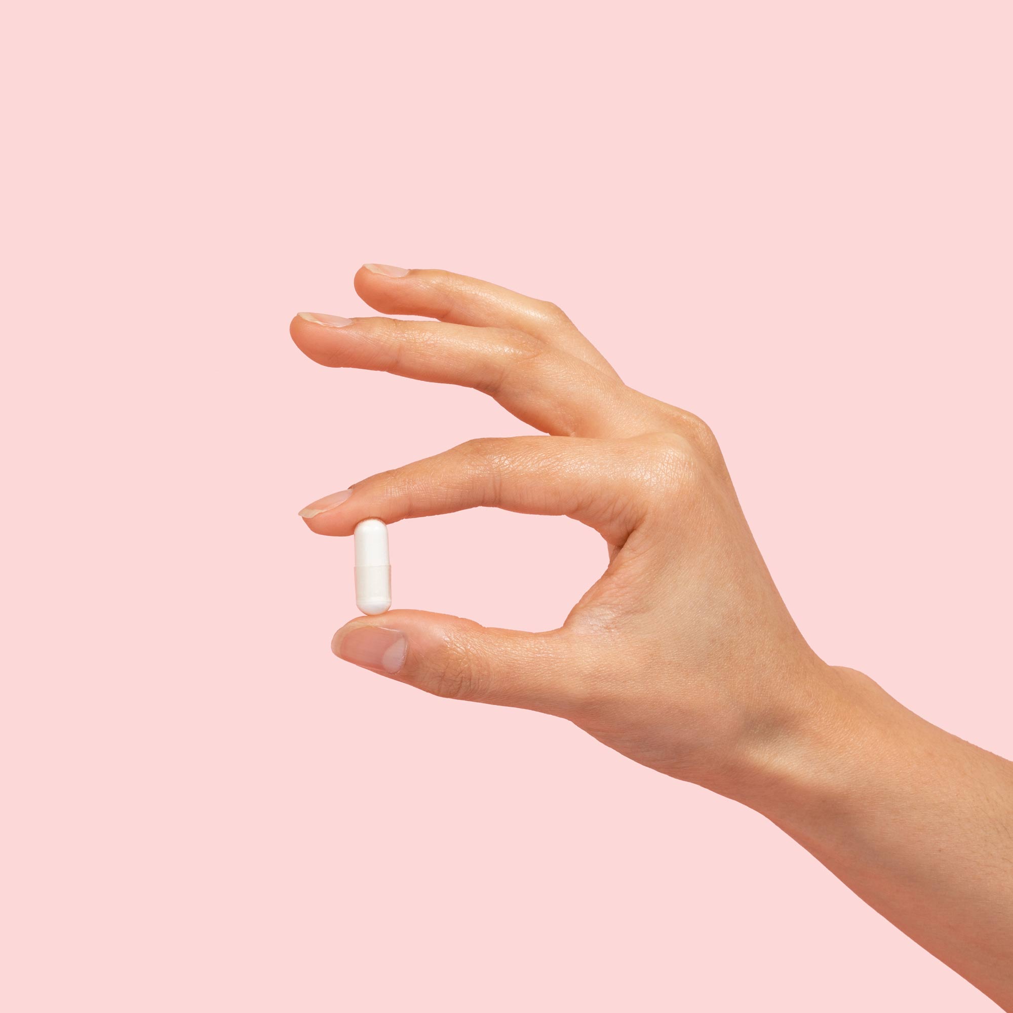 Hand holding lysine capsule on pink background