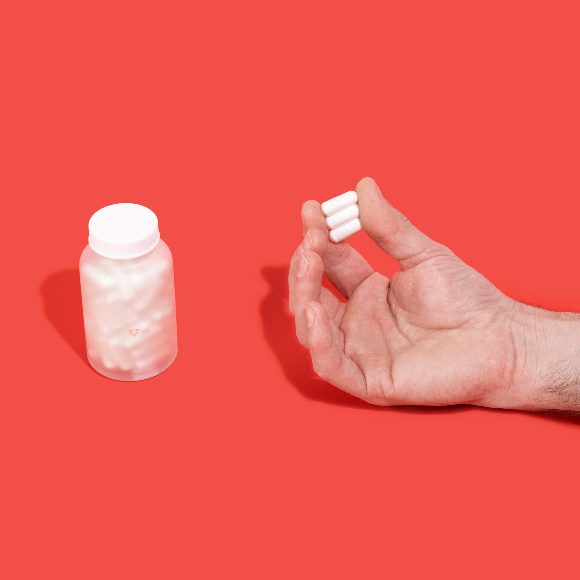 Hand holding lysine capsules next to jar on red background