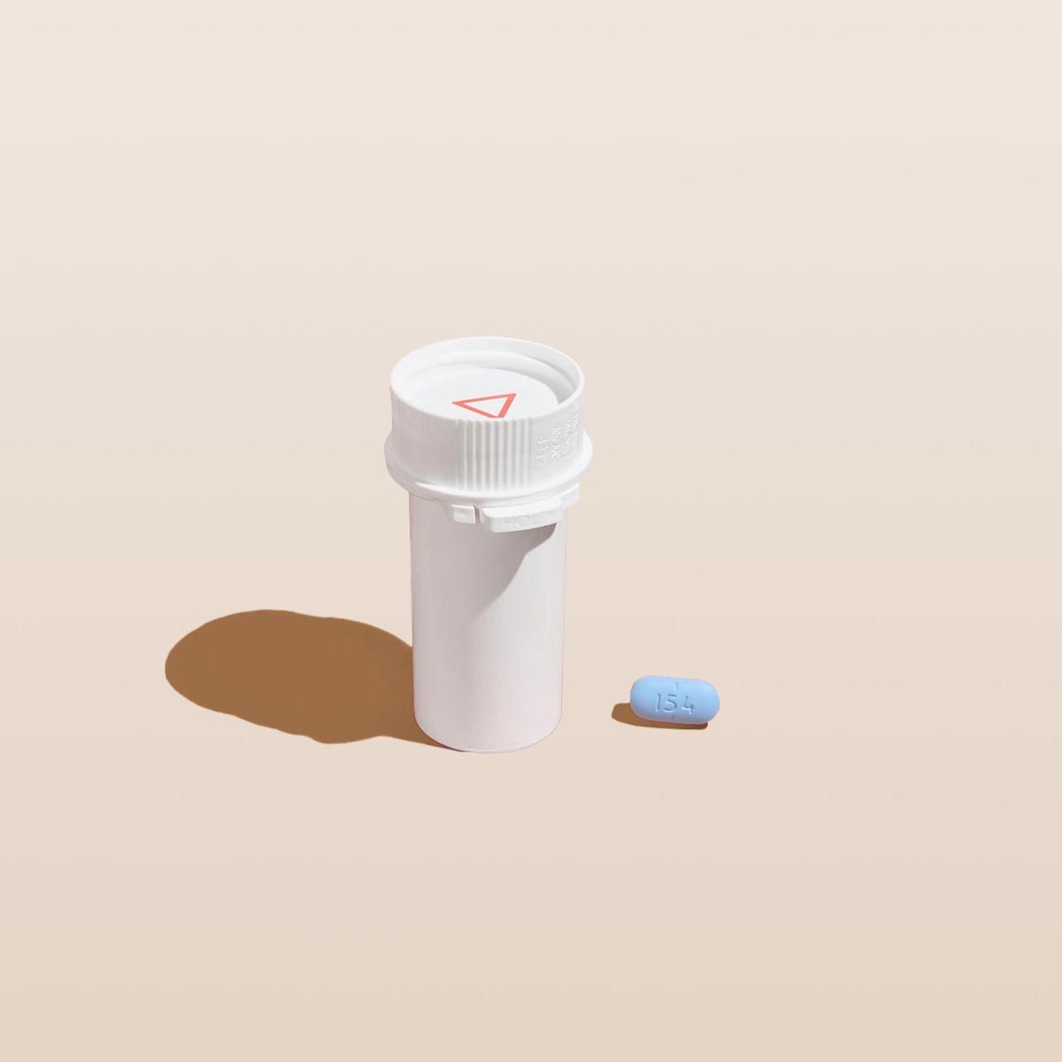 A pill vial with a blue pill on a cream surface