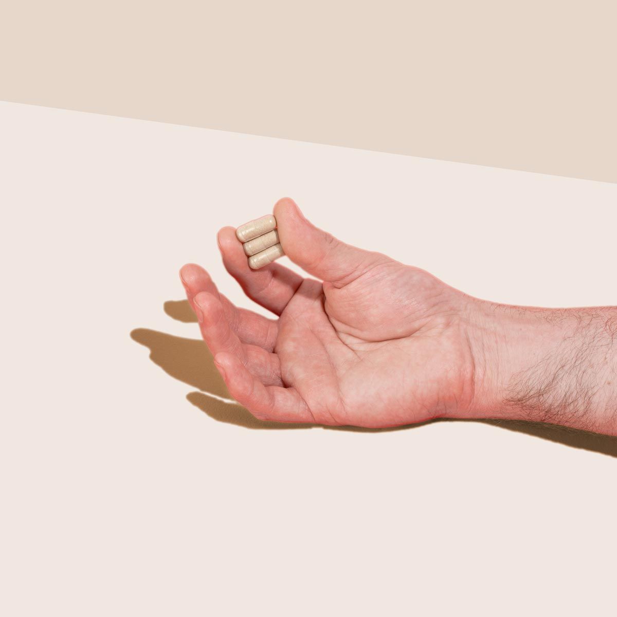 A person's hand holding 3 pills with a cream background