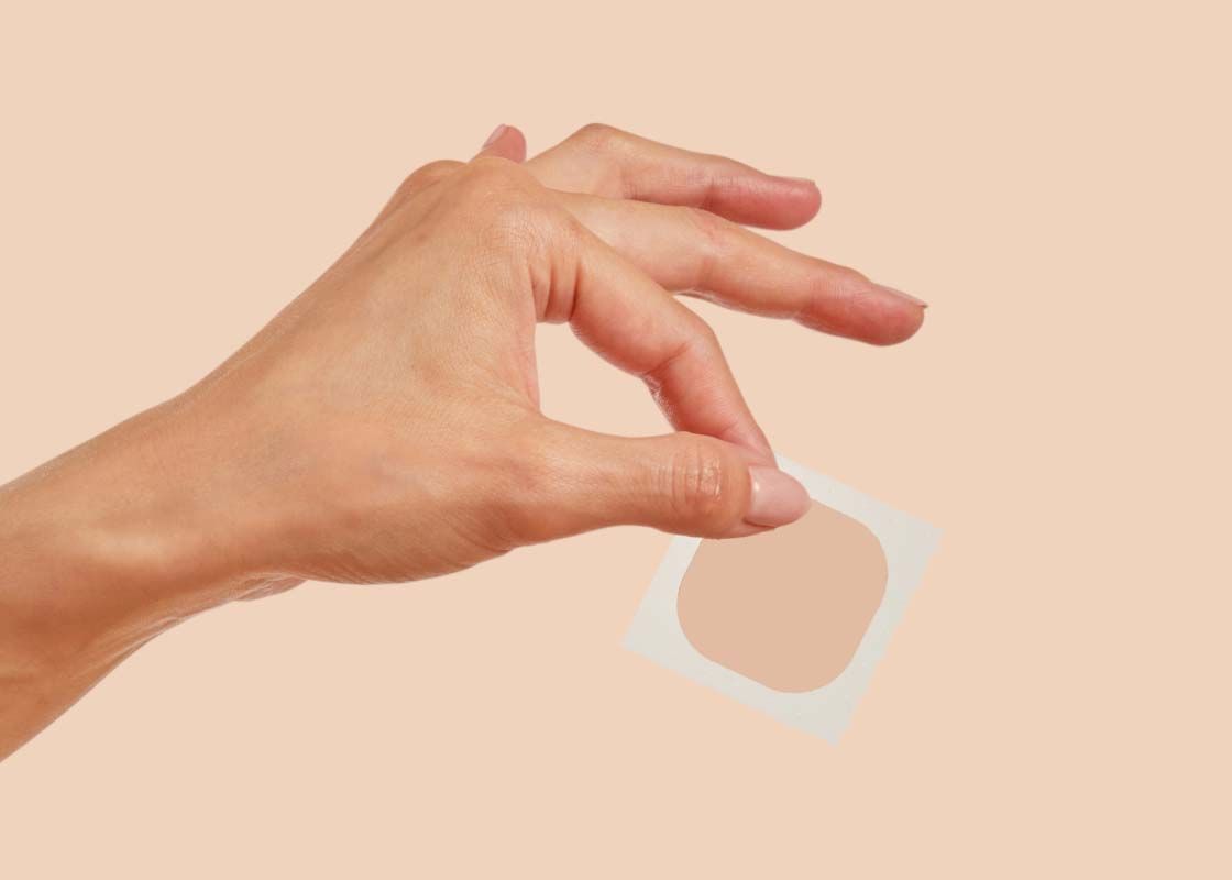 A woman's hand holding a small Wisp patch in front of a cream background