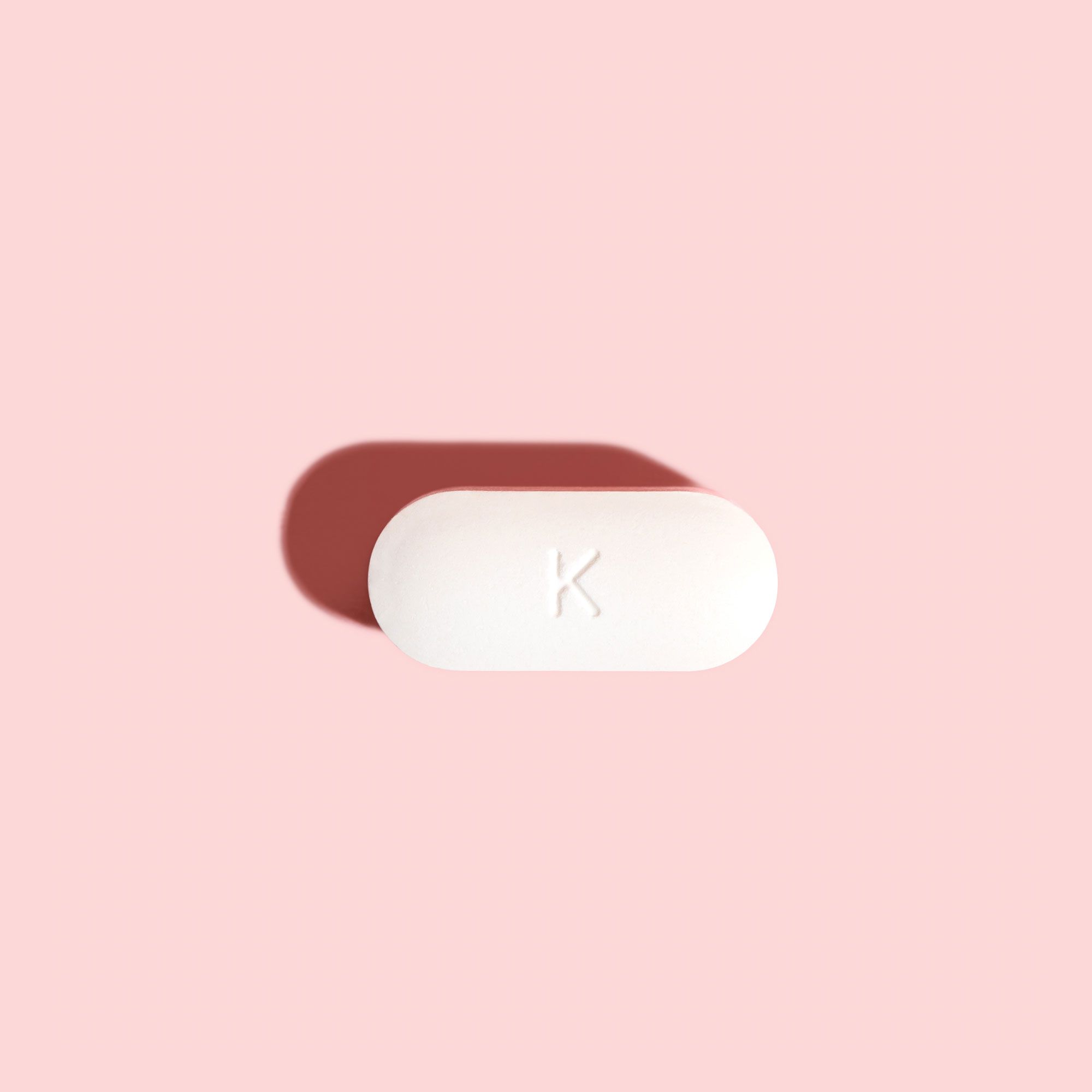 Single BV antibiotic tablet to treat bacterial vaginosis on a pink background and red surface