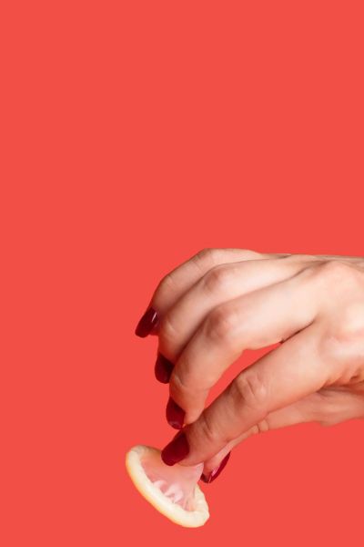 Person's hand holding a condom with a red background