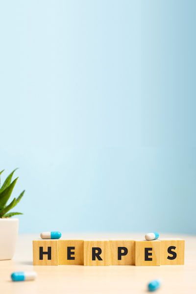 The word Herpes spelled out on wooden blocks with blue and white pills, a plant and a blue background