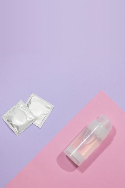 Bottle of clear liquid and 2 condoms on a pink and purple background