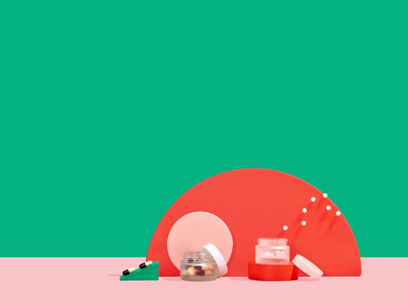 Two small Wisp glass jars with pills floating out on colorful abstract shapes with a green and pink background