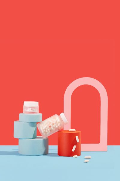 A tall Wisp glass jar with pills pouring out balanced on colorful abstract shapes with a light blue and red background