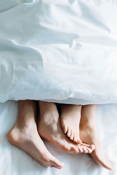 A couple's feet sticking out from underneath a white comforter