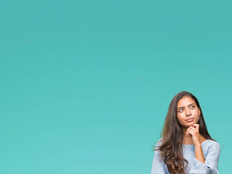 A woman with brown hair wearing a gray sweater has her hand on her chin in contemplation in front of a teal background