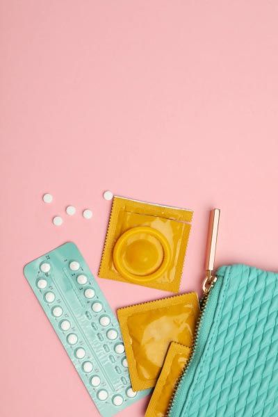 A green pouch with condoms and birth control pills spilling out on a pink surface