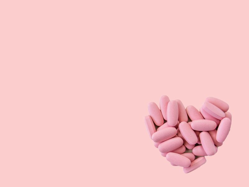 Pink oval-shaped pills grouped together in the shape of a heart on a pink surface