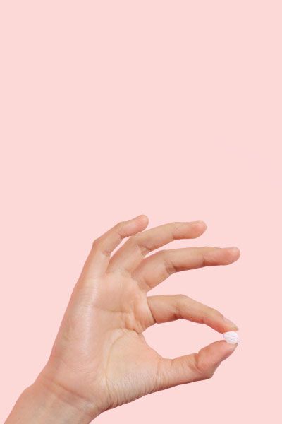 Hand holding a single Fluconazole pill with a pink background