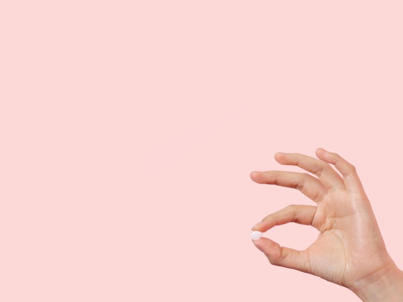 Hand holding a single Fluconazole pill with a pink background