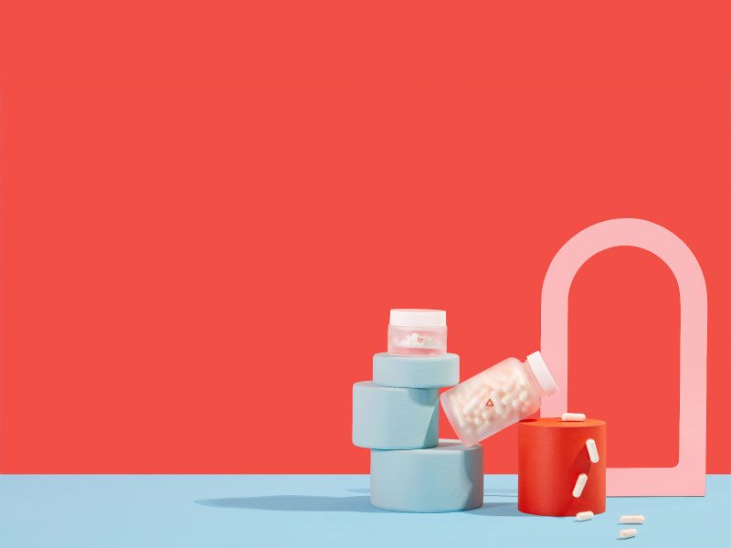 Two Wisp glass jars balancing on colorful abstract shapes will pills spilling out on a red and blue background