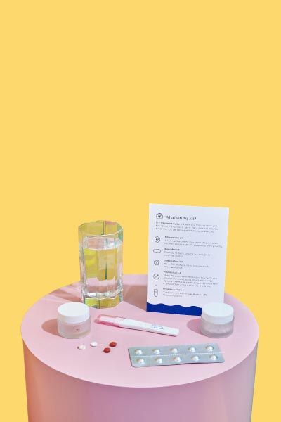 A pink nightstand with Wisp online abortion medications, treatment guide, and a glass of water, with yellow and green walls