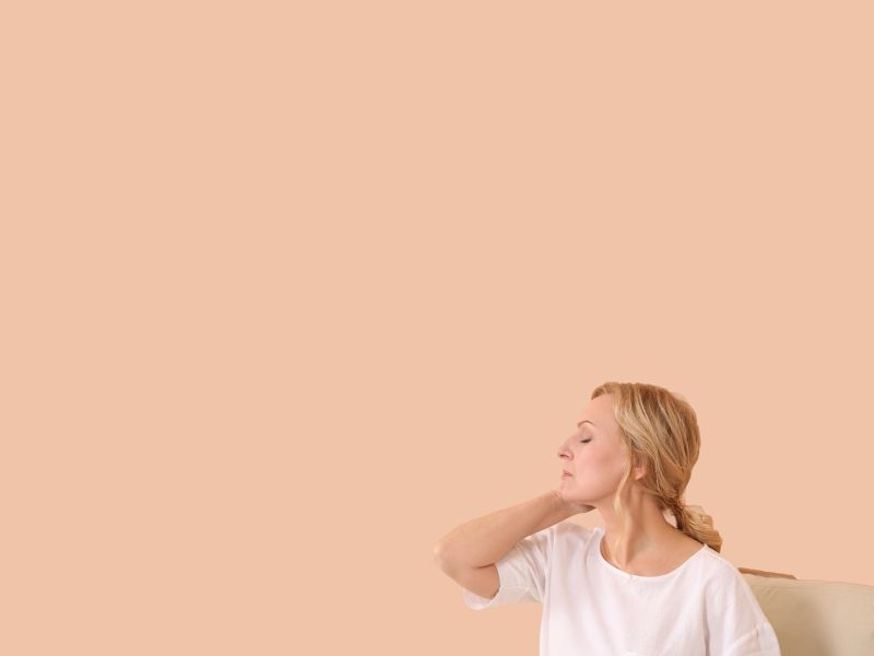 A woman with blonde hair and wearing a white shirt has her hand on the back of her neck and looks stressed