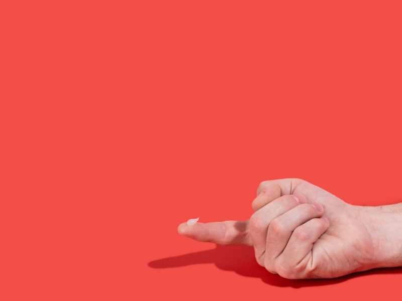 Man's hand with Acyclovir cream on his index finger with a red background