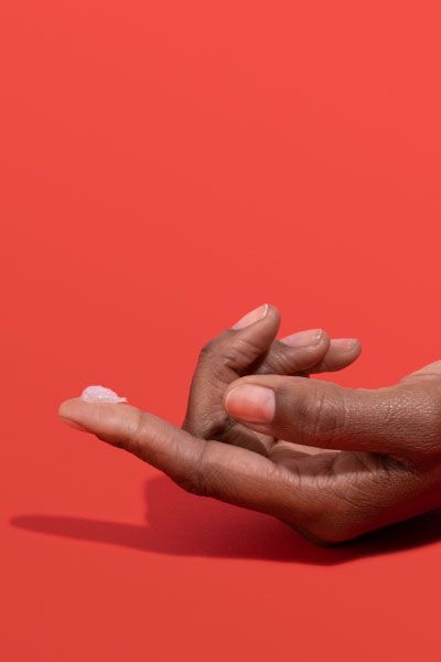 Woman's hand with Acyclovir cream on her fingertip with a red background