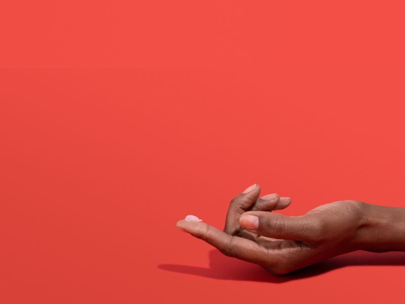 Woman's hand with Acyclovir cream on her fingertip with a red background