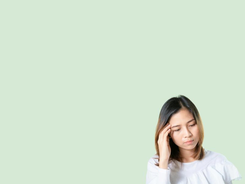 A woman wearing a white shirt has her hand on her temple in front of a green background