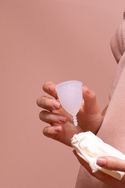 A woman wearing a sweatshirt and holding a menstrual cup