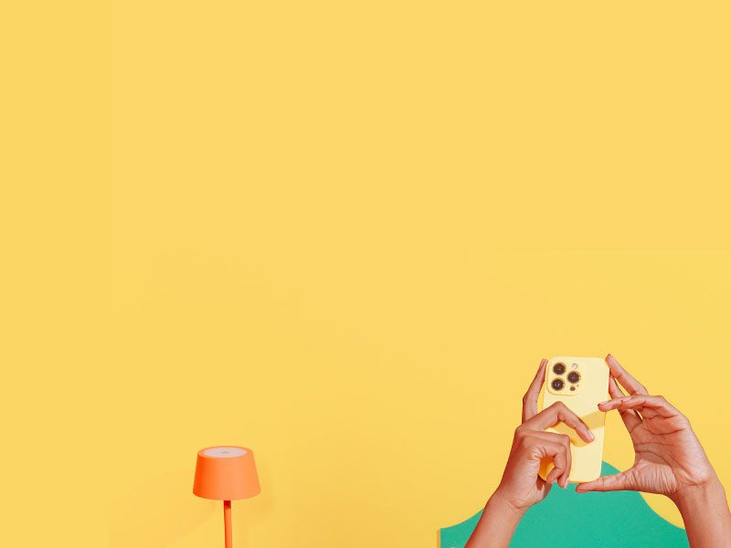 Female in bed ordering medication on her phone with a pink nightstand, orange lamp and Wisp glass medication jar with an orange and yellow background