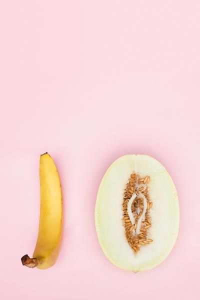 A banana and a cut open vulva-shapes fruit on a pink surface
