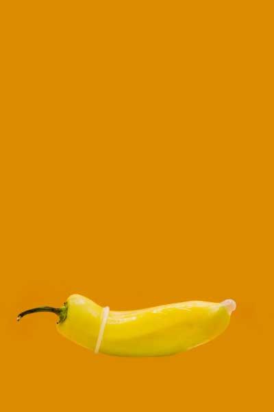 A yellow pepper with a condom on it in front of an orange background
