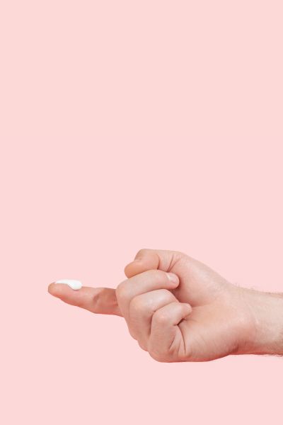 Man's hand with lidocaine cream on the index fingertip with a pink background