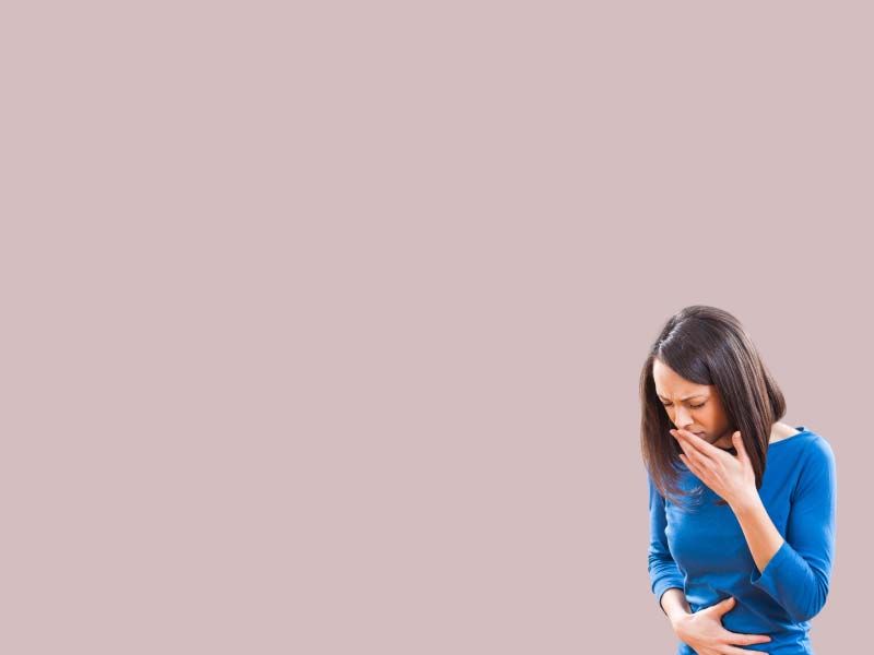 A woman wearing a blue shirt has one hand over her abdomen and one over her mouth indicating nausea