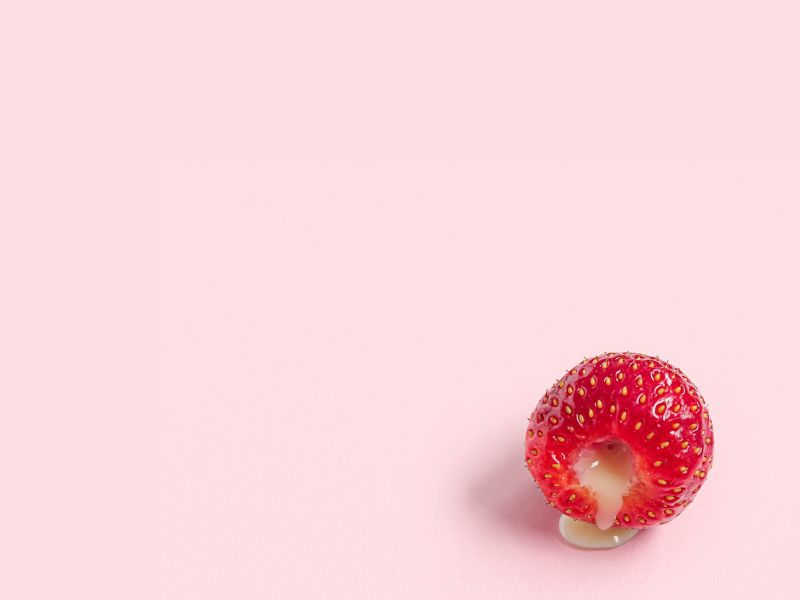 a raspberry oozing a creamy filling on a pink background