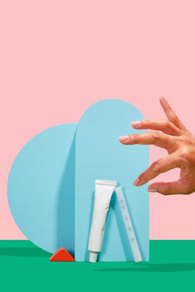 A hand is reaching for a tube of Wisp vaginal moisturizer and applicator with colorful abstract shapes on a pink and green background