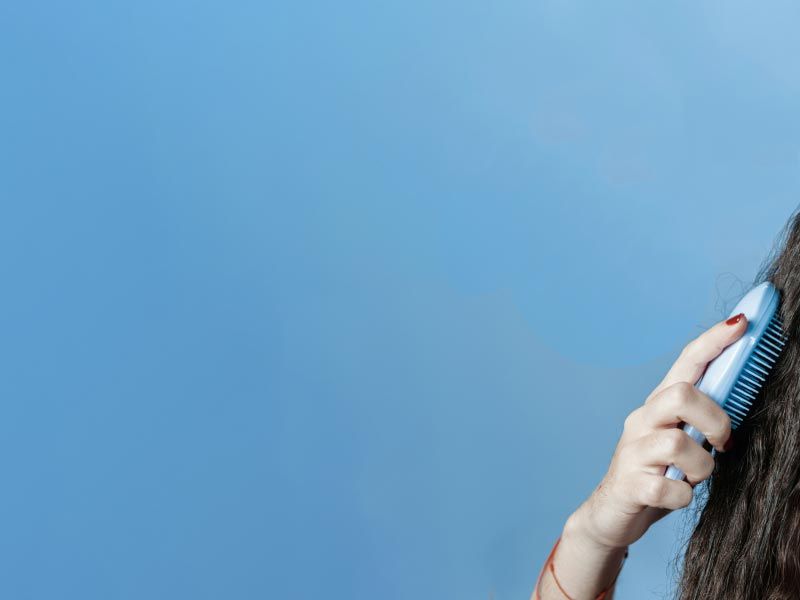 A person brushing their curly, frizzy hair in front of a blue background