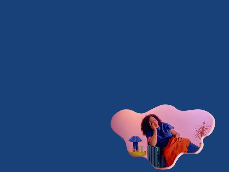 A woman sitting on a blue sofa with her hand on her face in discomfort