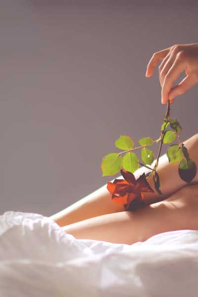 A woman laying on a bed dangling a rose over her legs