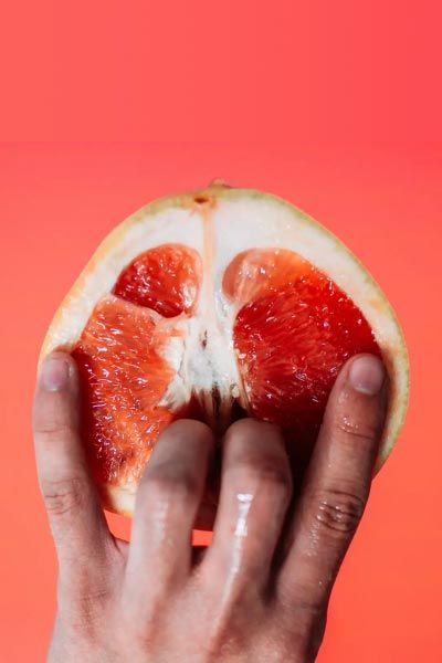 A hand suggestively holding a cut open grapefruit on a reddish background