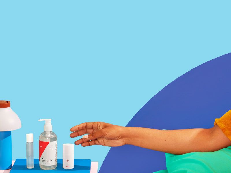 Woman's hand reaching for Wisp Balancing Wash, Harmonizing Lube, and OMG Cream on a pink nightstand with a blue lamp and green and blue walls