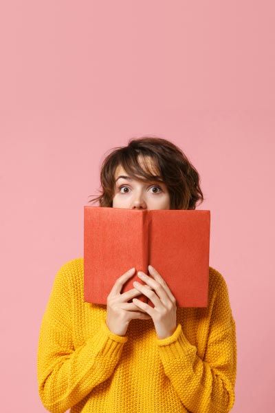 A woman wearing a yellow sweater and holding a brown book with a surprised look on her face